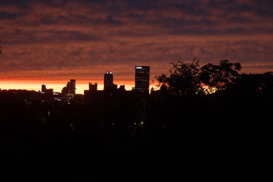 Pittsburgh's skyline in silhouette against a deep orange sunset.