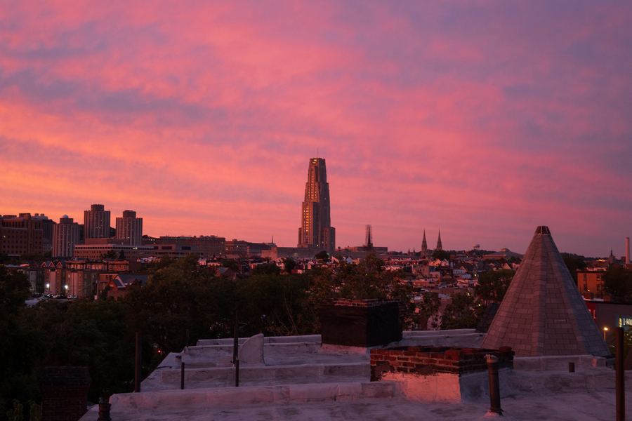 Pittsburgh at sunset under a magenta sky, the Cathedral of Learning rising above the rooftops.